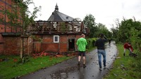 Orang-orang berdiri di depan sebuah rumah yang rusak akibat diterjang angin puting beliung di Lippstadt, Jerman. (Friso Gentsch/dpa via AP)