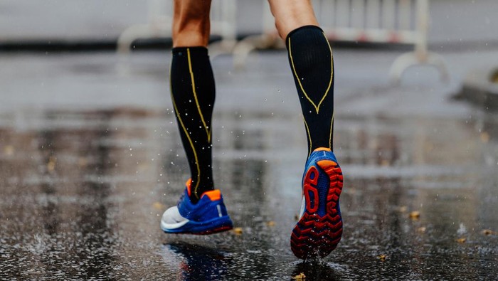 feet male runner in compression socks running on wet asphalt
