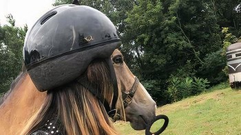 Bukan kuda pakai helm, tapi wanita berhelm berdiri di samping kuda.