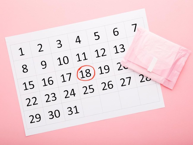 Sick Asian young woman lying in bed holding stomach in pain