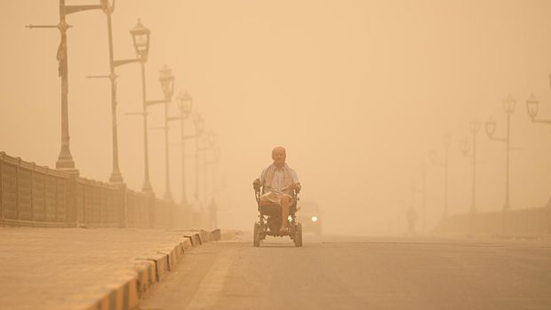 Seorang pria menggunakan kursi rodanya di jalan saat badai pasir di Baghdad,  Irak, Senin (23/5/2022). (AP Photo/Hadi Mizban)