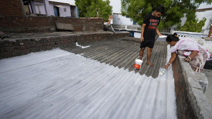 A person paints his rooftop with cool white reflective paint which brings down indoor temperature in summer, in Ahmedabad, India, Monday, May 23, 2022. The intense heat wave sweeping through South Asia was made more likely due to climate change and it is a sign of things to come. An analysis by international scientists said that this heat wave was made 30-times more likely because of climate change, and future warming would make heat waves more common and hotter in the future. (AP Photo/Ajit Solanki)