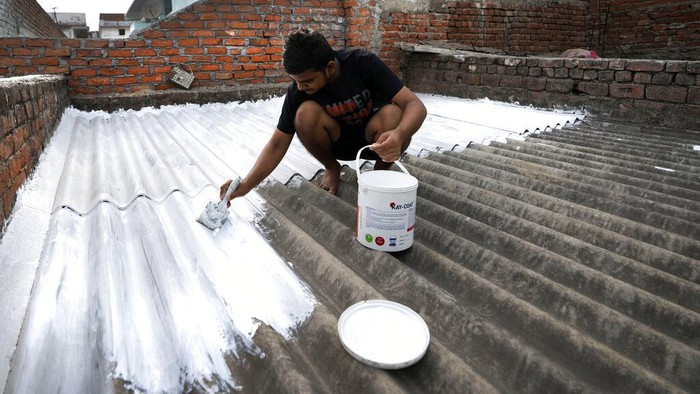 A person paints his rooftop with cool white reflective paint which brings down indoor temperature in summer, in Ahmedabad, India, Monday, May 23, 2022. The intense heat wave sweeping through South Asia was made more likely due to climate change and it is a sign of things to come. An analysis by international scientists said that this heat wave was made 30-times more likely because of climate change, and future warming would make heat waves more common and hotter in the future. (AP Photo/Ajit Solanki)