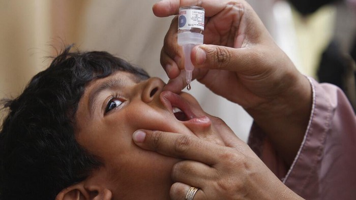 Upaya Bebas Polio Untuk Anak-anak Pakistan Policemen provide security for a health worker administering a polio vaccine to a child in Karachi, Pakistan, Monday, May 23, 2022. Pakistan launched a new anti-polio drive on Monday, more than a week after officials detected the third case so far this year in the country's northwestern region bordering Afghanistan. (AP Photo/Fareed Khan)