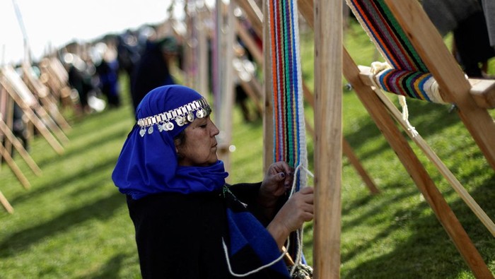 Wanita Chile Pecahkan Rekor Bikin Kain Tenun Terpanjang Dunia Indigenous Mapuche women work in their looms while seeking to break a world record by gathering loom weavings that together will measure more than 1 kilometre in length in Puerto Saavedra, Chile, May 21, 2022. REUTERS/Juan Gonzalez