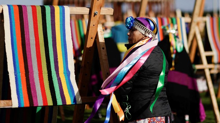 Wanita Chile Pecahkan Rekor Bikin Kain Tenun Terpanjang Dunia Indigenous Mapuche women work in their looms while seeking to break a world record by gathering loom weavings that together will measure more than 1 kilometre in length in Puerto Saavedra, Chile, May 21, 2022. REUTERS/Juan Gonzalez