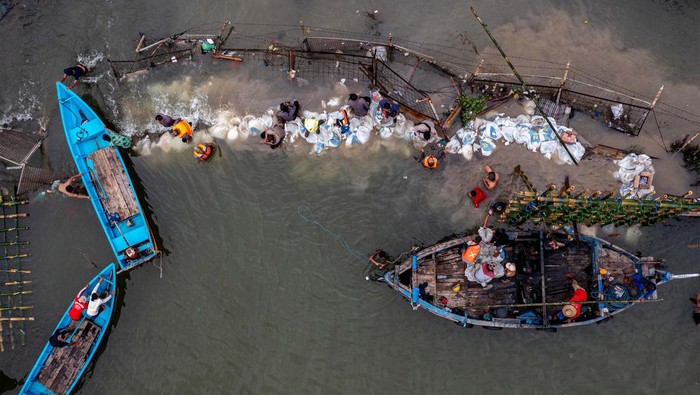 Personel kepolisian dari Polsek Kesatuan Pelaksanaan Pengamanan Pelabuhan (KP3) Tanjung Emas Semarang bersama warga dan relawan bergotong royong menutup tembok kawasan industri atau tanggul yang jebol dengan konstruksi pagar bambu dan karung berisi pasir dan batu di kawasan industri Pelabuhan Tanjung Emas Semarang, Jawa Tengah, Rabu (25/5/2022). PT Pelindo (Persero) Regional 3 Tanjung Emas Semarang menyiapkan 3.600 karung berisi pasir dan batu serta pagar bambu untuk membuat tanggul darurat guna menutup tanggul yang jebol. ANTARA FOTO/Aji Styawan/tom.
