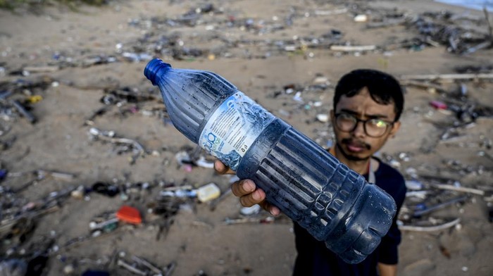 SAMPAH PLASTIK DI PANTAI TNUK Seorang jurnalis memperlihatkan botol sampah plastik produksi luar negeri yang terbawa arus di bibir pantai selatan, kawasan Taman Nasional Ujung Kulon (TNUK), Pandeglang, Banten, Senin (16/5/2022). Banyaknya sampah plastik di kawasan tersebut diperkirakan dapat menyebabkan perubahan perilaku satwa di wilayah tersebut salah satunya badak jawa yang disinyalir tidak lagi terlihat di muara dekat pantai selatan. ANTARA FOTO/Muhammad Adimaja/tom.