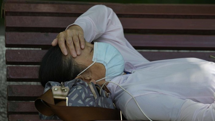 A resident wearing a mask naps on a bench, Monday, May 30, 2022, in Beijing. (AP Photo/Ng Han Guan)