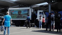Orang-orang nampak berkumpul di depan layar yang menyiarkan program berita TV Rusia di titik distribusi bantuan kemanusiaan selama konflik Ukraina-Rusia di kota pelabuhan selatan Mariupol.