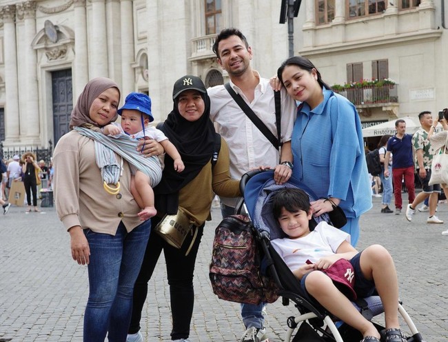 Jika pengasuh Rayyanza, Lala tampil dengan topi dan tas bermerek, Rini justru terlihat berpenampilan sederhana. Sambil menggendong Rayyanza, Rini terlihat hanya mengenakan kaos lengan panjang berwarna coklat dengan celana jeans berwarna biru. Penampilannya itu dilengkapi dengan hijab berwarna coklat. Foto: Instagram