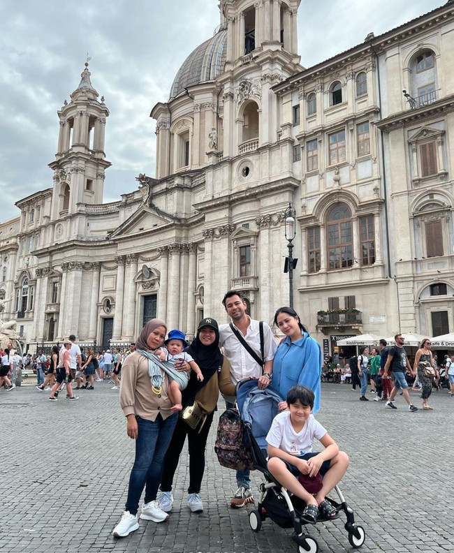 Begini penampilan Rini saat berpose bersama Lala dan keluarga Raffi Ahmad di Roma, Italia. Sambil menggendong Rayyanza, Rini terlihat konsisten berpenampilan sederhana. Foto: Instagram