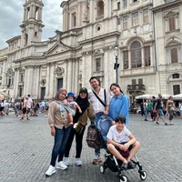 Begini penampilan Rini saat berpose bersama Lala dan keluarga Raffi Ahmad di Roma, Italia. Sambil menggendong Rayyanza, Rini terlihat konsisten berpenampilan sederhana. Foto: Instagram