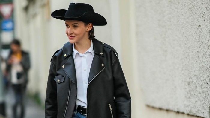 MILAN, ITALY - FEBRUARY 23: A guest wears a black felt hat, a white shirt, a black shiny leather oversized zipper jacket, blue denim cigarette jeans pants, a black shiny leather handbag from Balenciaga, black and white leather yoke and metallic pointed block heels ankle boot, outside the Alberta Ferretti fashion show, during the Milan Fashion Week Fall/Winter 2022/2023 on February 23, 2022 in Milan, Italy. (Photo by Edward Berthelot/Getty Images)