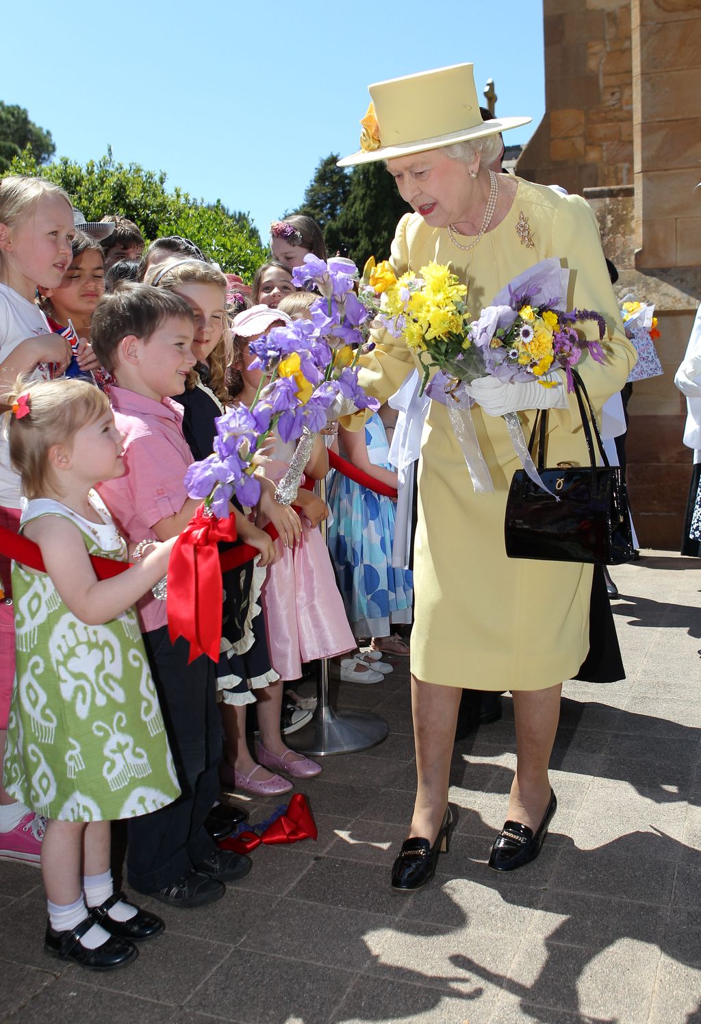 Gaya Ratu Elizabeth II Daur Ulang Baju Britain's Queen Elizabeth II (R) receives flowers from children after attending church services at St. John's in Canberra on October 23, 2011. The queen is in Australia for her 16th visit to the former penal colony on what will perhaps be the 85-year-old monarch's last tour Down Under. AFP PHOTO / POOL / ALEX COPPEL (Photo credit should read ALEX COPPEL/AFP via Getty Images)