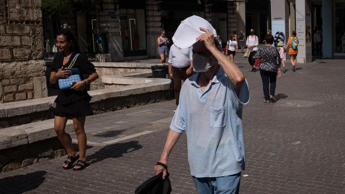 A man puts the newspaper for protection from the sun at Ermou street in the center if Athens, Greece on June 1, 2022. Greece was in high temperatures today. (Photo by Nikolas Kokovlis/NurPhoto via Getty Images)
