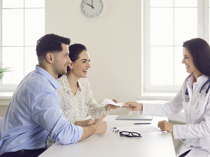 1364023041 Consulting family doctor at clinic. Happy patients take therapy prescription that general practitioner gives. Future parents get good health exam result. Infertile married couple have success with IVF