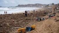 Orang-orang berdiri di pantai yang tertutup sampah dan puing-puing setelah Badai Agatha, di Zipolite, negara bagian Oaxaca, Meksiko, Rabu, (1/6/2022).