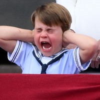 Suasana mendadak bergemuruh saat pesawat melakukan aksi fly-past di atas Istana. Pangeran Louis yang kaget mendadak menutup telinganya. (Foto: AFP via Getty Images/DANIEL LEAL)