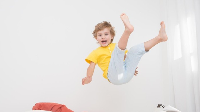 Cheerful little boy  jumping on bed at home