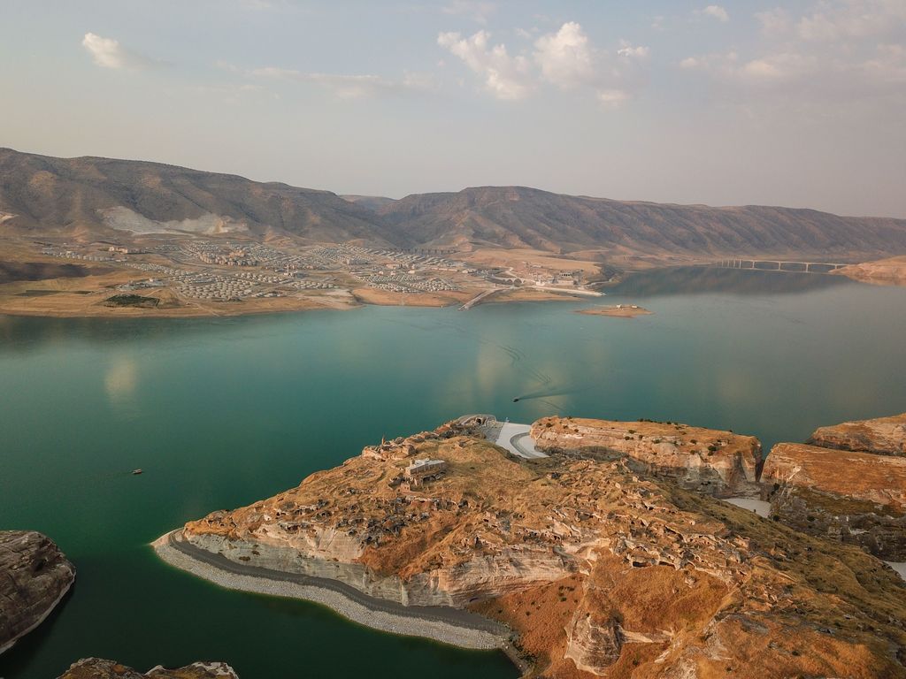 This picture taken on August 3, 2020, shows the Il?su Dam separating the  newly constructed Hasankeyf town and the remains of the ancient town (foreground) of the same name and its archaeological sites which were flooded as part of the Il?su Dam project located along the Tigris River in the Batman Province in southeastern Turkey. - Despite years of protests by residents and activists, the town on the banks of the Tigris River disappeared under water as part of a controversial dam project. To encourage tourism, swimming is allowed and people can enjoy a boat tours. (Photo by BULENT KILIC / AFP) (Photo by BULENT KILIC/AFP via Getty Images)
