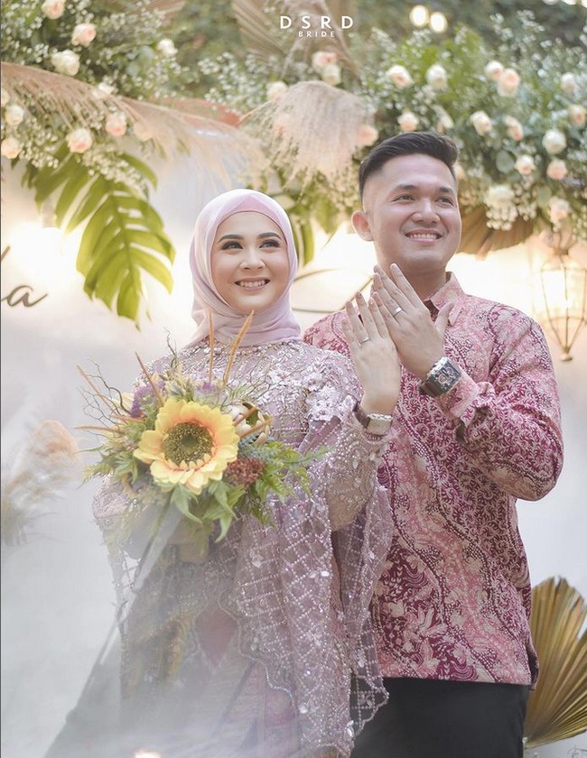 Kesha tampil dengan menggunakan kebaya lamaran hijab model baju kurung warna pink dari Kilau Arti dan memakai kain lilit motif batik. Kesha tampil anggun dengan menggunakan hijab segi empat bahan pollycotton yang dililit rapi ke belakang dan memakai inner warna pink. Sedangkan Adhi Permana memakai batik dengan warna senada. Foto: Dok. Instagram @kesharatuliu05.