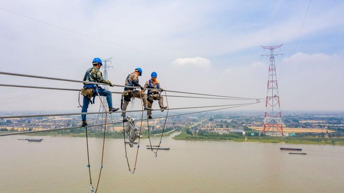 TAIZHOU, CHINA - JUNE 01: Workers install electric wires on the 385-meter-high worlds tallest transmission tower by the side of Yangtze River during construction of a 500-kilovolt ultra-high voltage (UHV) power line on June 1, 2022 in Taizhou, Jiangsu Province of China. (Photo by Shi Jun/VCG via Getty Images)