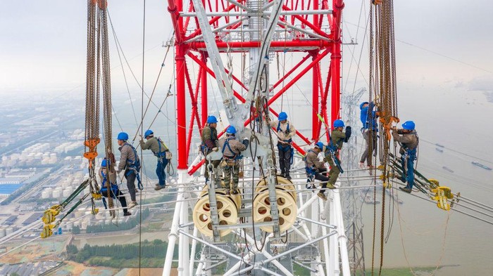 TAIZHOU, CHINA - JUNE 01: Workers install electric wires on the 385-meter-high world's tallest transmission tower by the side of Yangtze River during construction of a 500-kilovolt ultra-high voltage (UHV) power line on June 1, 2022 in Taizhou, Jiangsu Province of China. (Photo by Shi Jun/VCG via Getty Images)
