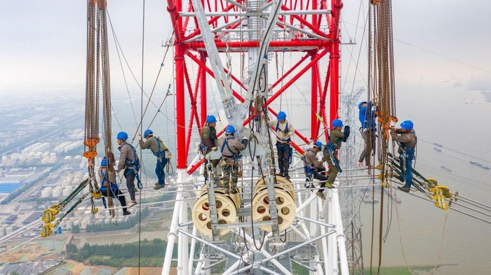 Pemasangan Kabel Listrik Tertinggi di Dunia TAIZHOU, CHINA - JUNE 01: Workers install electric wires on the 385-meter-high world's tallest transmission tower by the side of Yangtze River during construction of a 500-kilovolt ultra-high voltage (UHV) power line on June 1, 2022 in Taizhou, Jiangsu Province of China. (Photo by Shi Jun/VCG via Getty Images)