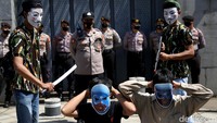 Tampak dua orang demonstran mengenakan topeng dan menodongkan senjata kepada dua orang lainnya yang berjongkok saat aksi teatrikal digelar di depan Kedubes China.
