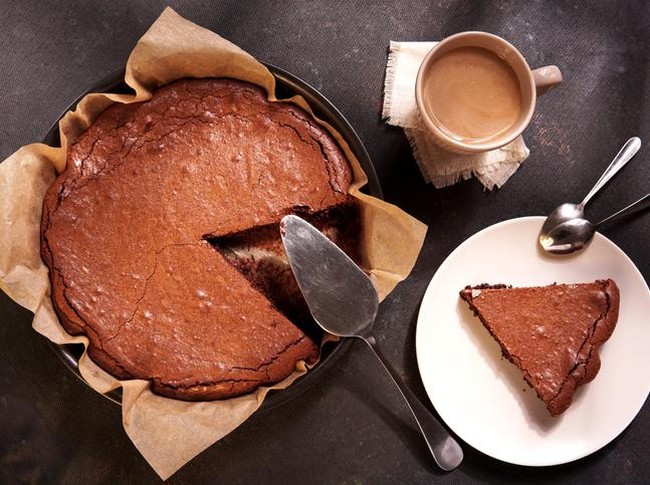 Homemade dark chocolate cake brownie in baking pan, mug with tea or coffee, chocolate on dark table with window light. Delicious bitter sweet and fudge.  Flat lay, top view, vintage style.
