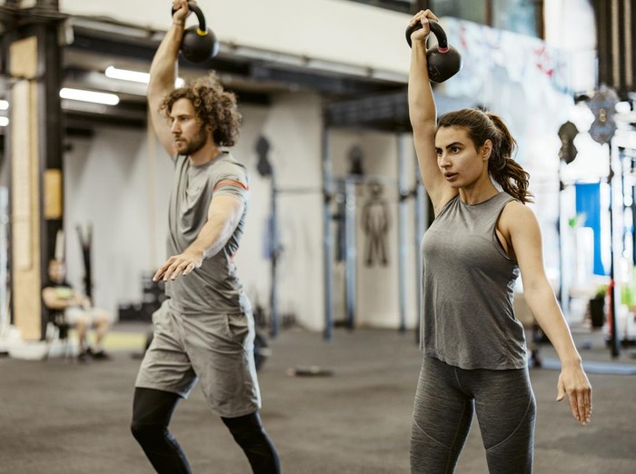 workout Two young athletes having cross training and doing split squats while lifting kettlebells in a health club