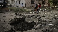 Sejumlah warga melihat kawah akibat hantaman rudal di depan gedung apartemen yang rusak di kota Loviansk, Donbas, Ukraina timur. (AFP/Aris Messinis).