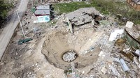 Sebuah kawah tampak menganga di sekitar rumah yang hancur di Desa Yatskivka, Ukraina timur. (AFP/Ronaldo Schemidt).