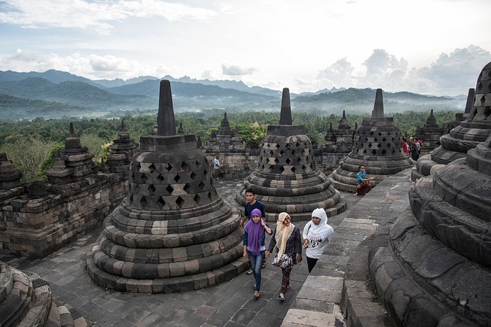 BOROBUDUR, SPECIAL REGION OF YOGYAKARTA, CE, INDONESIA - 2015/04/19: Tourists walk through stupas at the  Borobudur temple. The temple, built in the 8th century, is one of the largest Buddhist monuments in the world. Probably due to the decline of Buddhism and the Javanese conversion to Islam, it was abandoned for centuries and covered with volcanic ashes and thick vegetation. The UNESCO inscribed the temple on its world heritage list in 1991. (Photo by Thierry Falise/LightRocket via Getty Images)