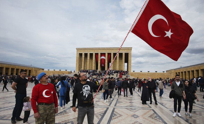 People sit at Kugulu public garden decorated with national flags and images of Turkeys founder Mustafa Kemal Ataturk, in Ankara, Turkey, Thursday, June 2, 2022. Turkey has sent a letter to the United Nations formally requesting that the country be referred to as 