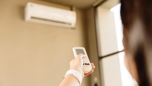 Closeup people using remote control adjust room temperature in home office pointing to Air conditioner in hot summer season.