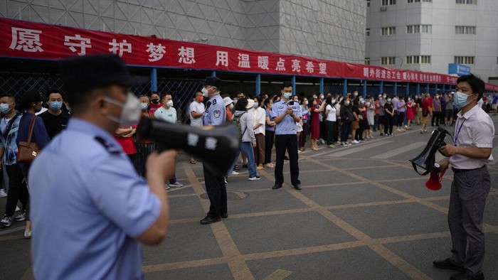 A volunteer directs students wearing face masks to enter a school for the first day of China's national college entrance examinations, known as the gaokao, in Beijing, Tuesday, June 7, 2022. More than 11 million high school students throughout China will take the annual college entrance exams which started on Tuesday after the country has just overcome severe COVID-19 outbreaks in Shanghai and Beijing, according to state media. (AP Photo/Andy Wong)