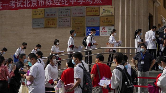 A volunteer directs students wearing face masks to enter a school for the first day of China's national college entrance examinations, known as the gaokao, in Beijing, Tuesday, June 7, 2022. More than 11 million high school students throughout China will take the annual college entrance exams which started on Tuesday after the country has just overcome severe COVID-19 outbreaks in Shanghai and Beijing, according to state media. (AP Photo/Andy Wong)