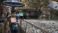 Sejumlah warga melintasi jembatan di sebelah sampah yang mengapung di Sungai Negro, yang permukaan airnya naik karena hujan di Manaus, negara bagian Amazonas, Brasil.