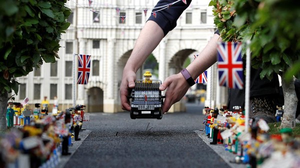 Model Ratu Elizabeth Inggris di dalam kendaraan dekat model Istana Buckingham.