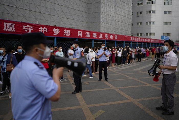 Virus Outbreak China College Entrance Exam A police officer stands watch as masked students line up to enter a school for the first day of China's national college entrance examinations, known as the gaokao, in Beijing, Tuesday, June 7, 2022. More than 11 million high school students throughout China will take the annual college entrance exams which started on Tuesday after the country has just overcome severe COVID-19 outbreaks in Shanghai and Beijing, according to state media. (AP Photo/Andy Wong)