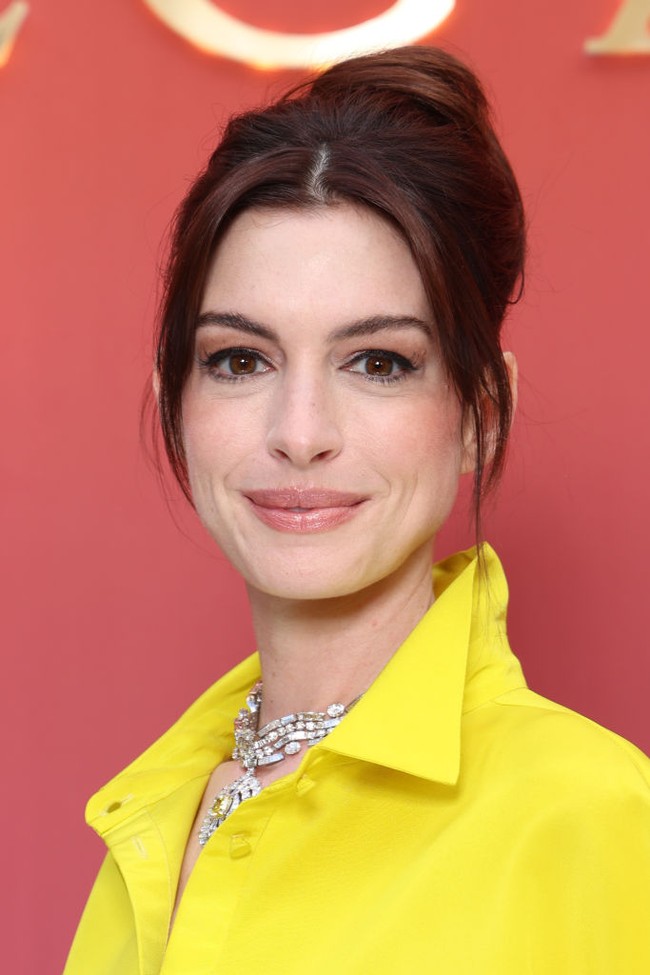 Anne Hathaway memilih riasan bergaya natural dengan nuansa nude peach. Sementara rambutnya disanggul tinggi, menyisakan poni panjang yang membingkai wajah cantiknya. Foto: Getty Images