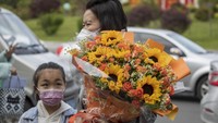 Tampak seorang wanita membawa bunga matahari saat menunggu anaknya mengikuti ujian masuk perguruan tinggi tahunan di Provinsi Jilin, China. (Zhu Wanchang/VCG/Getty Images).  