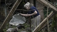 Seorang nenek itu membersihkan puing-puing di halaman rumahnya.