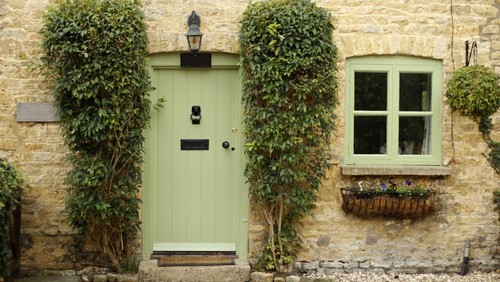 A front of a cottage with a green door and window.