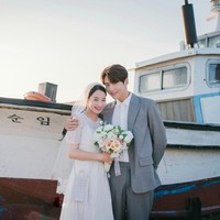 Pasangan drama Korea Hometown Cha Cha Cha ini tak kalah manis karena dibantu warga Gongjin saat foto pernikahan. Shin Min Ah memakai gaun sederhana dengan tatanan rambut low bun, dilengkapi veil. Perhiasannya pun tak begitu mewah. Dia dirangkul Kim Seon Ho yang memakai setelan jas abu-abu bermotif kotak-kotak. Foto: dok. tvN
