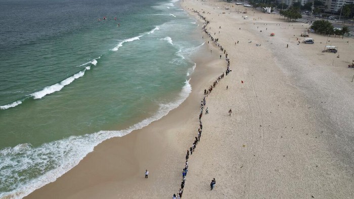 Warga Brasil Ramai-ramai Bersihkan Pantai Copacabana People create a line along Copacabana beach for a symbolic group hug with the sea on World Oceans Day in Rio de Janeiro, Brazil, Wednesday, June 8, 2022. The Route Brasil organization called for people to gather for the event coined