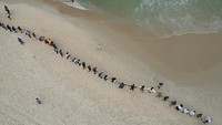 Orang-orang terlihat berbaris membuat pelukan dengan laut sebagai simbolis kepedulian terhadap pencemaran laut.
