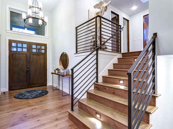 Chic entrance foyer with high ceiling and wide staircase with lights and contemporary railing. New Custom built home interior.
